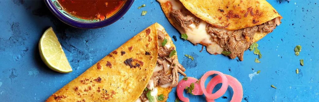 Overhead of birria tacos on blue background