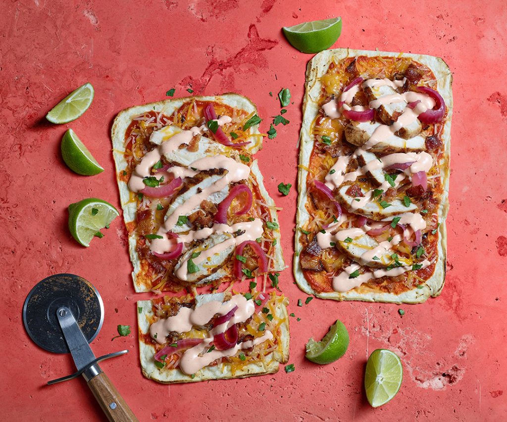 Overhead image of Mexican pizzas with a pizza cutter and lime garnishes