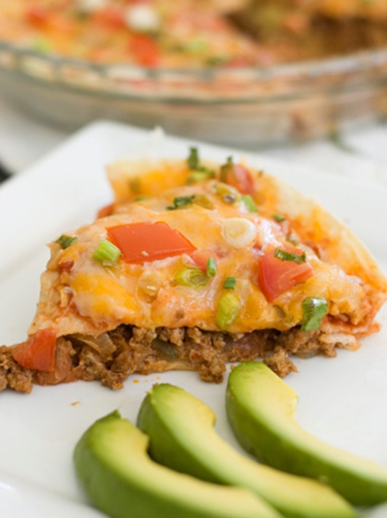 Slice of Mexican pizza with sliced avocado on the side