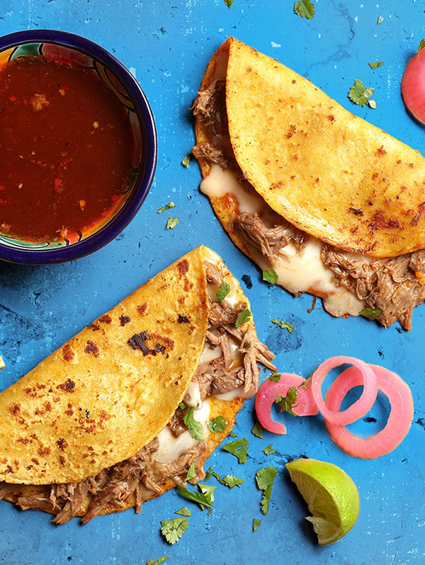 Birria tacos on a bright blue surface