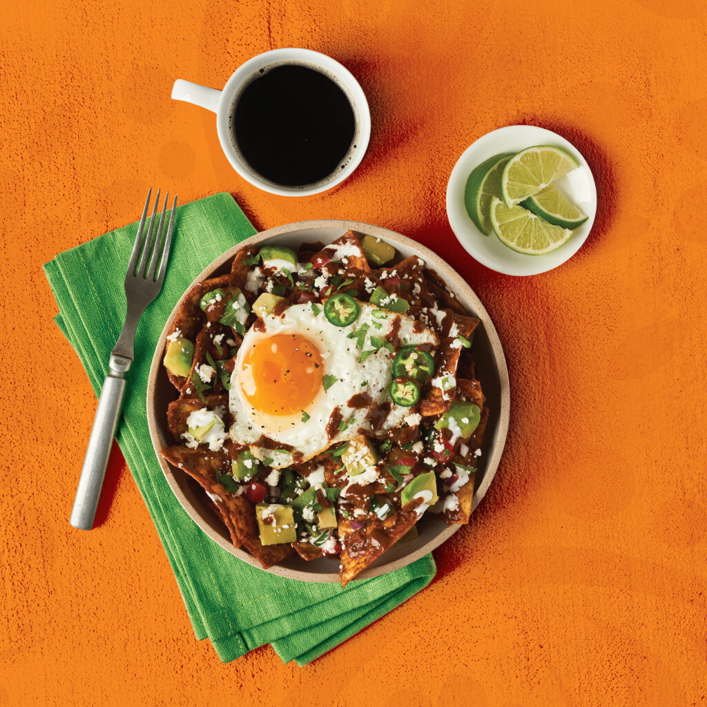 Overhead shot of breakfast chilaquiles in a bowl with a cup of coffee and lime wedges.