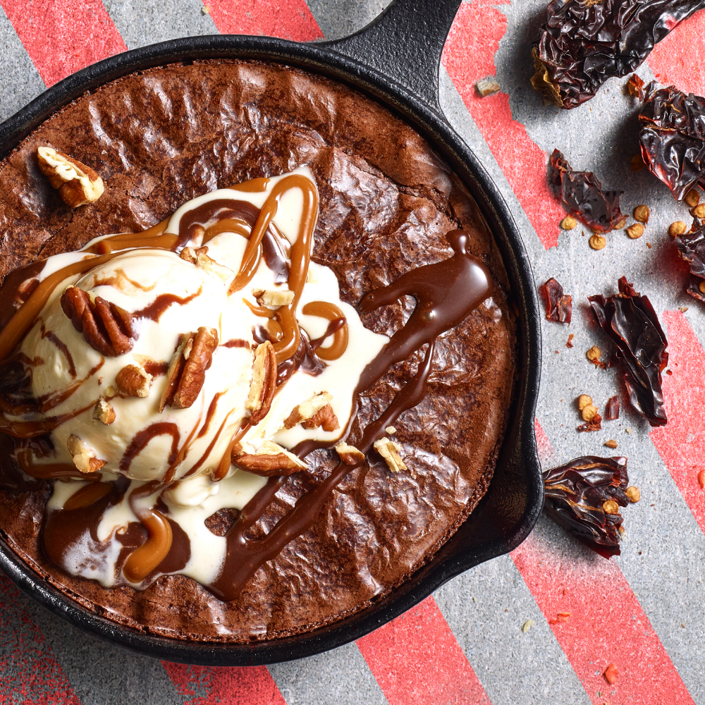 Brownie in a skillet topped with ice cream and sauces