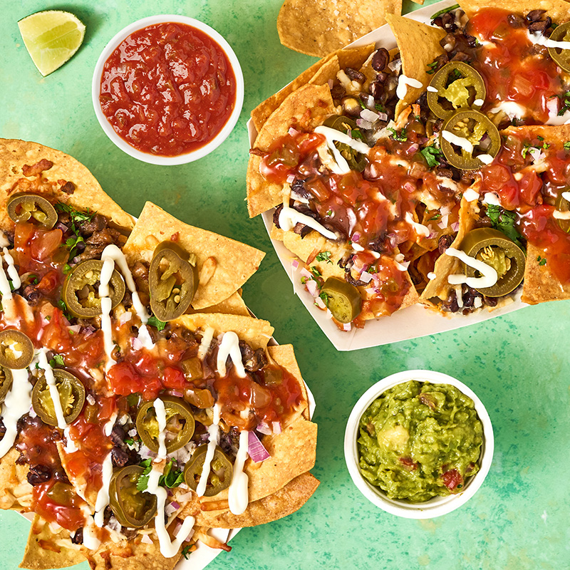 Carne Asada Nachos in paper boats with sides of salsa, guacamole and lime wedges 