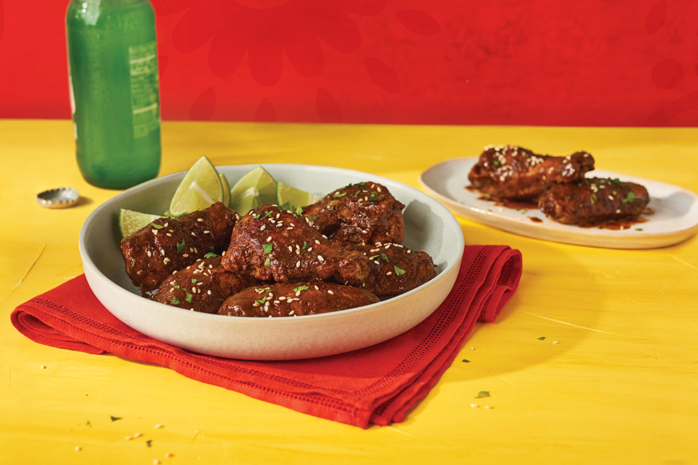 Mole chicken wings on a platter with a side of lime wedges